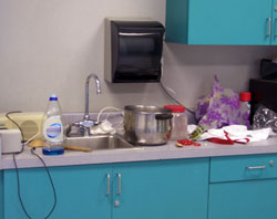 a sink in a theater green room with spilled water and electrical applicances plugged in.