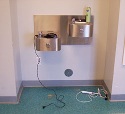a drinking faucet with an electrical applicance placed in it and the cord is in the aisle way.